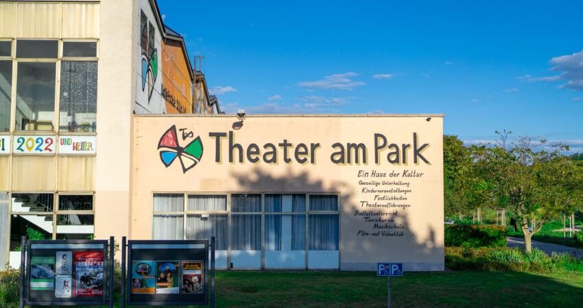 Theater am Park, im Hintergrund der blaue Himmel unigrüne Bäume.