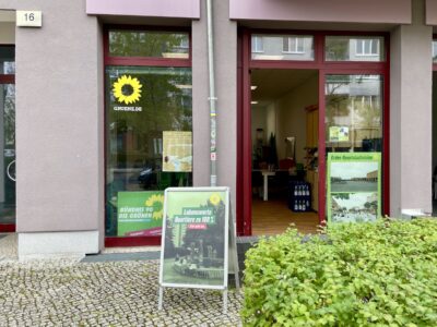 Die Kreisgeschäftsstelle der Grünen Marzahn-Hellersdorf ist geöffnet. Sie ist durch das Parteilogo an der Fensterscheibe erkennbar. Vor der Tür steht ein Aussteller mit einem Parteiplakat.