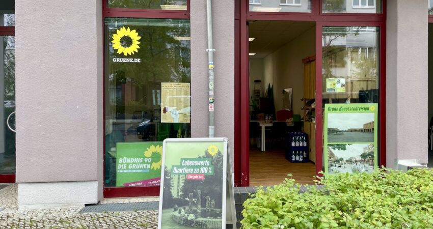 Die Kreisgeschäftsstelle der Grünen Marzahn-Hellersdorf ist geöffnet. Sie ist durch das Parteilogo an der Fensterscheibe erkennbar. Vor der Tür steht ein Aussteller mit einem Parteiplakat.
